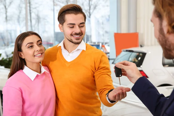 Venditore di auto dando la chiave per coppia in concessionaria — Foto Stock