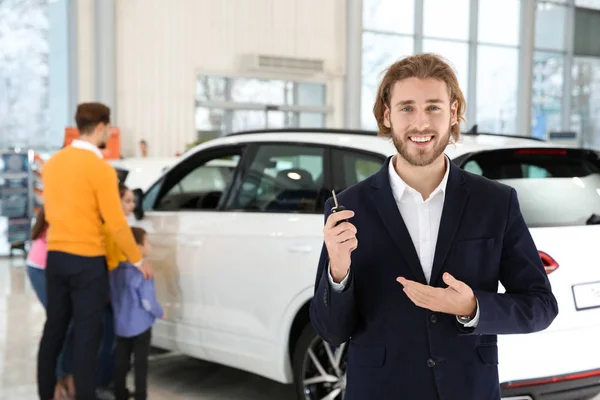 Vendedor de coches con la llave y la familia borrosa cerca de auto en el fondo — Foto de Stock