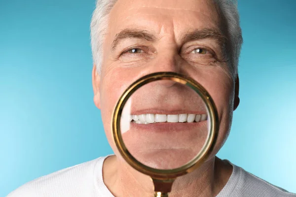 Mature man with healthy teeth and magnifier on color background, closeup — Stock Photo, Image