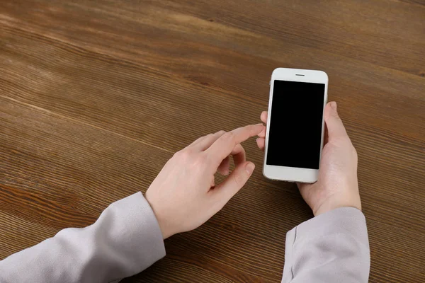 Vrouw met behulp van de mobiele telefoon aan tafel, close-up met ruimte voor ontwerp — Stockfoto