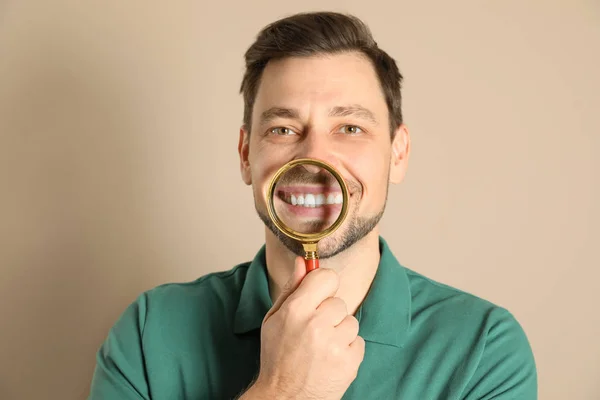 Smiling man with perfect teeth and magnifier on color background — Stock Photo, Image