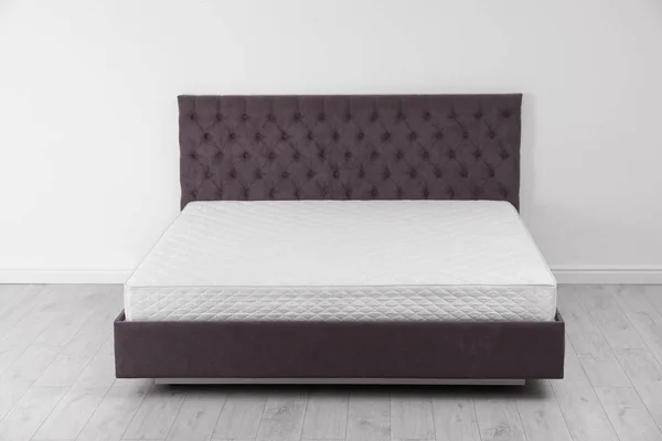 Άνετο κρεβάτι με καινούργιο στρώμα κοντά σε τοίχο στο δωμάτιο. Υγιή ύπνο — Φωτογραφία Αρχείου