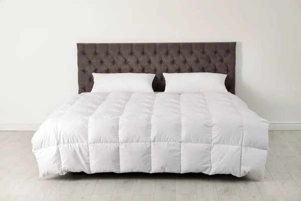 Wygodne łóżko z nowym materacem w pobliżu ściany w pokoju. Zdrowy sen — Zdjęcie stockowe