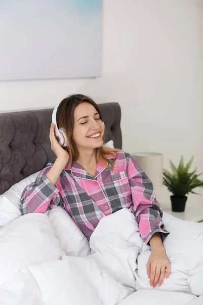 ベッドで音楽を楽しむヘッドフォンを持つ若い女性 — ストック写真