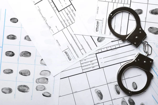 Наручники и листы с отпечатками пальцев, вид сверху. Уголовное расследование — стоковое фото