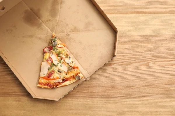 Cardboard box with pizza piece on wooden background, top view with space for text