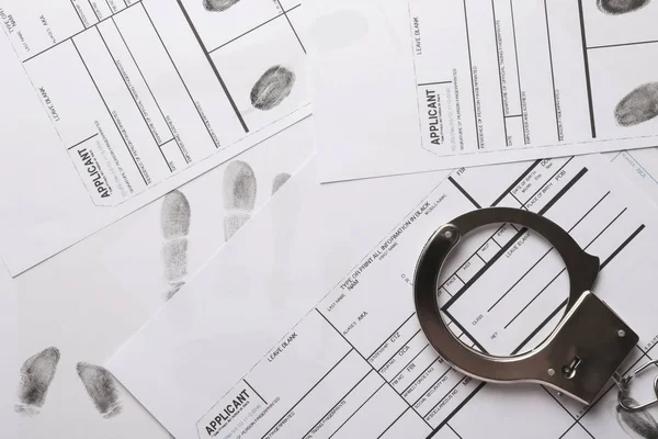 Наручники и листы с отпечатками пальцев, вид сверху. Уголовное расследование — стоковое фото