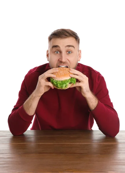 Jovem comendo hambúrguer saboroso na mesa no fundo branco — Fotografia de Stock