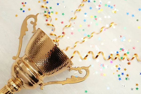 Goldener Pokal mit Luftschlangen auf Holzgrund. Raum für Text — Stockfoto
