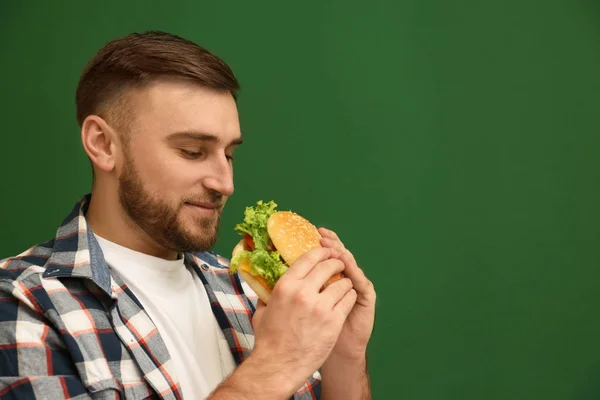 Young man eating tasty burger on color background. Space for text — Stock Photo, Image
