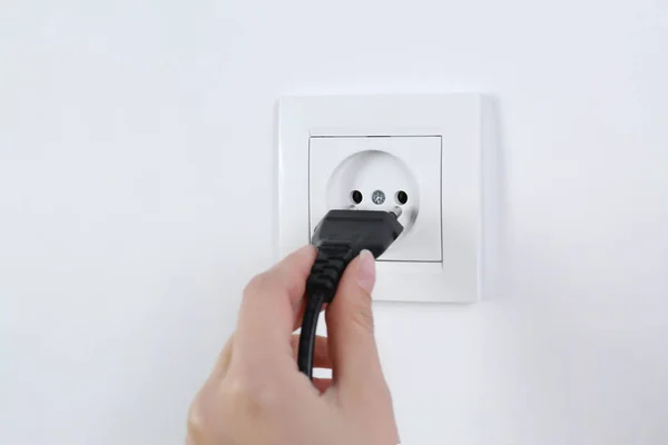 Mujer poniendo enchufe en toma de corriente sobre fondo blanco, primer plano. Equipos de electricista — Foto de Stock