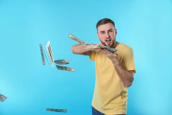 Happy young man throwing money on color background — Stock Photo, Image