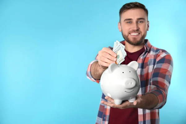 Onnellinen nuori mies laittaa rahaa säästöpossu väri tausta. Tekstitila — kuvapankkivalokuva