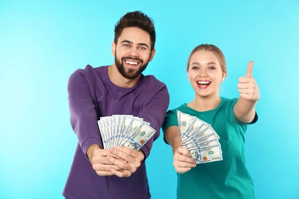 Happy young couple with money on color background — Stock Photo, Image