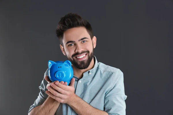 Piggy bank a szürke háttér boldog fiatalember portréja. Pénz megtakarítási — Stock Fotó