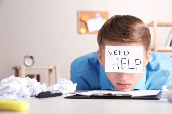 Ein junger Mann mit Zettel braucht am Arbeitsplatz Hilfe auf der Stirn. Raum für Text — Stockfoto