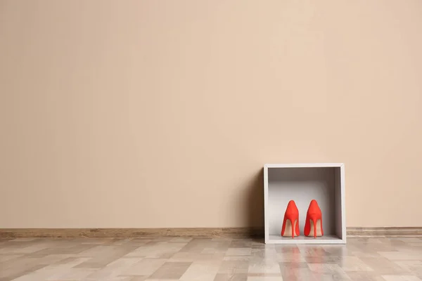 Modern cabinet with high heeled shoes near color wall, space for text