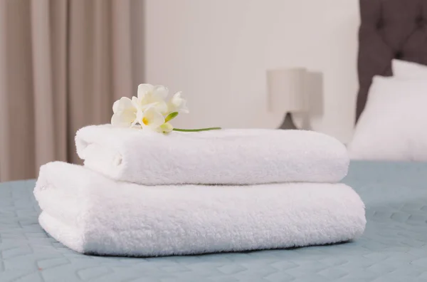 Pilha de toalhas frescas com flores na cama no quarto do hotel — Fotografia de Stock