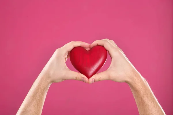 Hombre sosteniendo el corazón decorativo en las manos sobre el fondo de color, primer plano — Foto de Stock