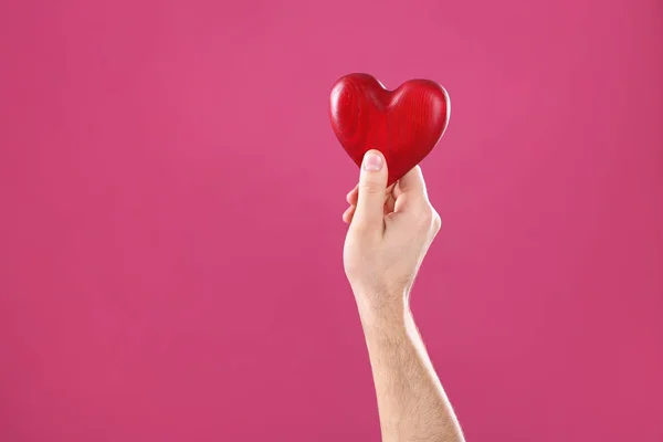 Hombre sosteniendo el corazón decorativo en la mano sobre fondo de color, espacio para el texto — Foto de Stock