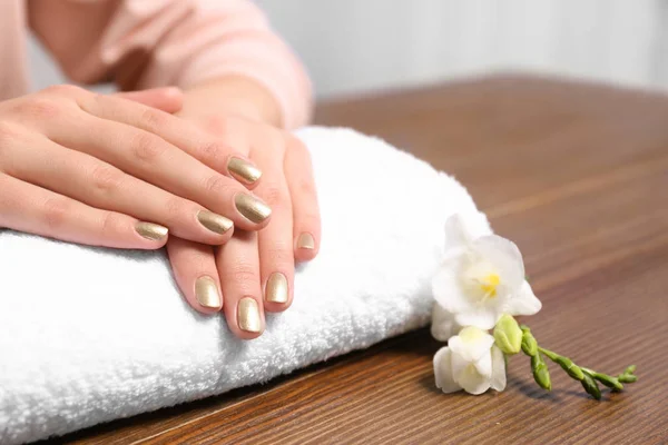 Mujer con manicura dorada en toalla enrollada en la mesa, primer plano. Tendencias de esmalte de uñas — Foto de Stock