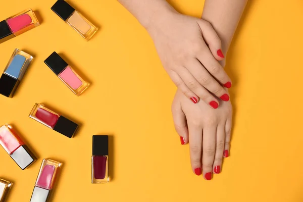 Mujer con manicura roja y botellas de esmalte de uñas sobre fondo de color, vista superior — Foto de Stock