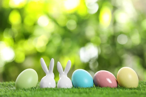 Keramická velikonoční zajíčky a barvená vejce na zelené trávě proti rozostřeného pozadí. Prostor pro text — Stock fotografie