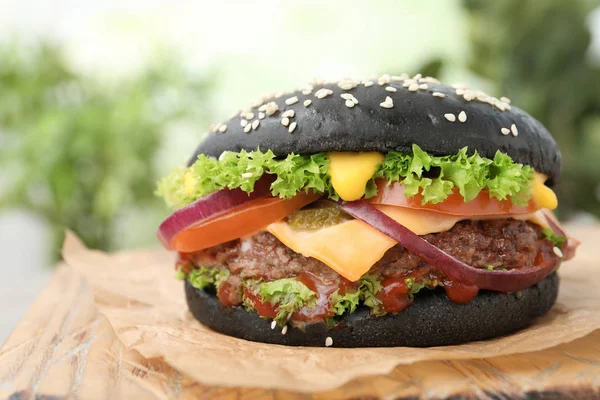 Deska s černým burger na rozmazané pozadí, closeup — Stock fotografie