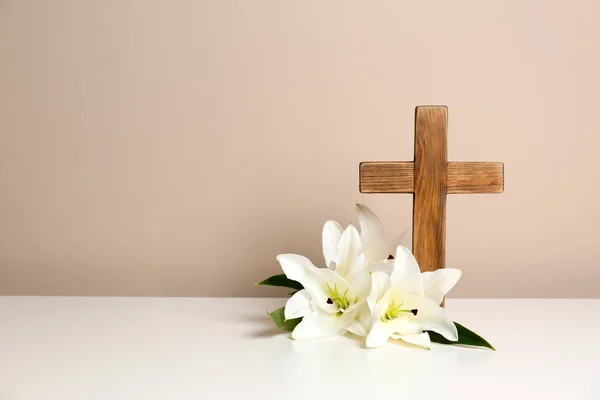 Композиція з дерев'яним хрестом і квітучими ліліями на столі на кольоровому фоні, простір для тексту — стокове фото