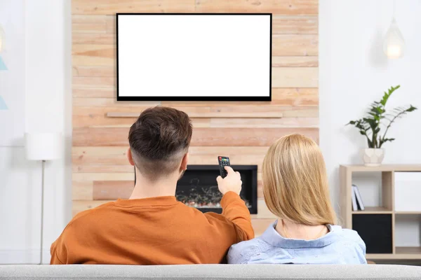 Couple watching TV on sofa in living room with decorative fireplace — Stock Photo, Image