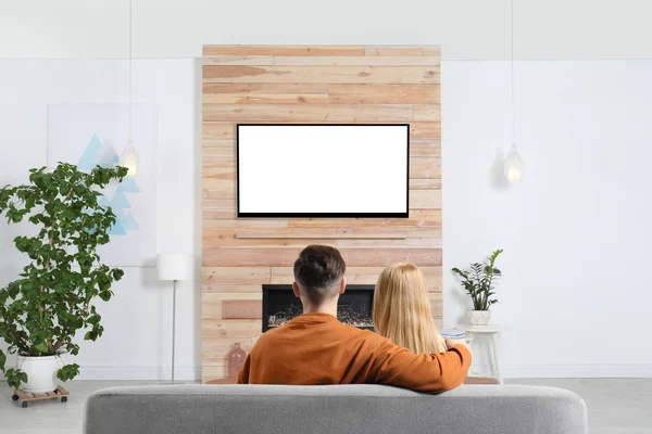 Couple regardant la télévision sur canapé dans le salon avec cheminée décorative — Photo