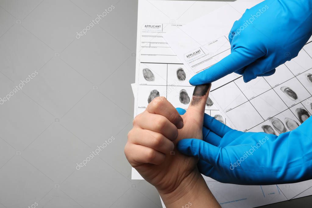 Investigator taking fingerprints of suspect on grey background, closeup with space for text. Criminal expertise