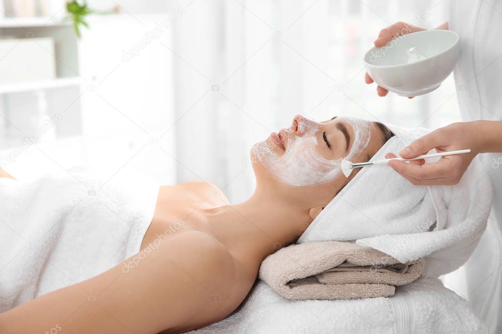 Cosmetologist applying mask on client's face in spa salon