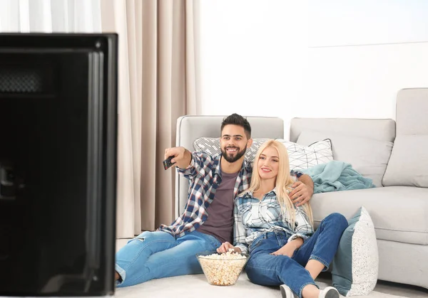 年轻夫妇拿着一碗爆米花在家里的地板上看电视 — 图库照片