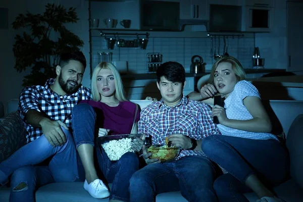 Młodzi przyjaciele z przekąskami, oglądania telewizji na kanapie w nocy — Zdjęcie stockowe