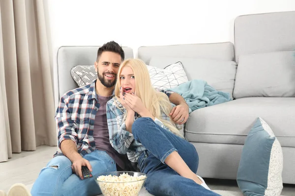 Jovem casal com tigela de pipoca assistindo TV no chão em casa — Fotografia de Stock