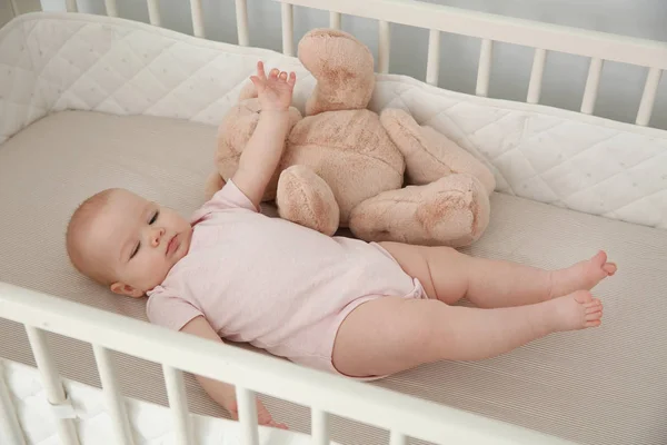 Niedliches kleines Mädchen mit Spielzeug in der Krippe zu Hause. Schlafenszeit — Stockfoto