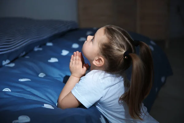 Liten flicka säger läggdags bön nära sängen i rummet på natten — Stockfoto