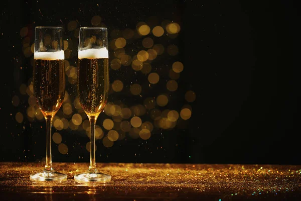 Ochelari de șampanie și sclipici aurii pe masă pe fundal neclar. Spațiu pentru text — Fotografie, imagine de stoc