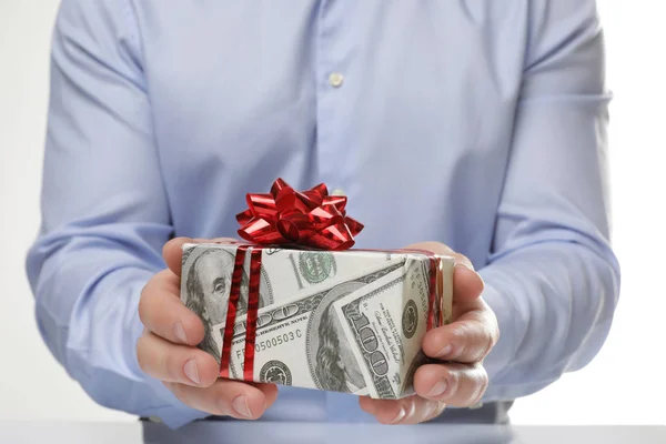Homem segurando caixa de presente envolto em papel decorativo com padrão de dólar no fundo branco, close-up — Fotografia de Stock