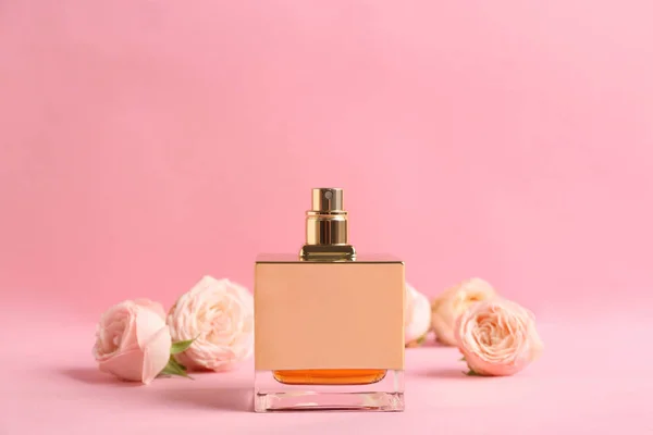Бутылка духов с красивыми розами на цветном фоне — стоковое фото