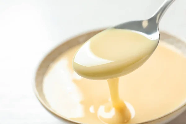 Spoon of pouring condensed milk over bowl on table, closeup with space for text. Dairy products — Stock Photo, Image