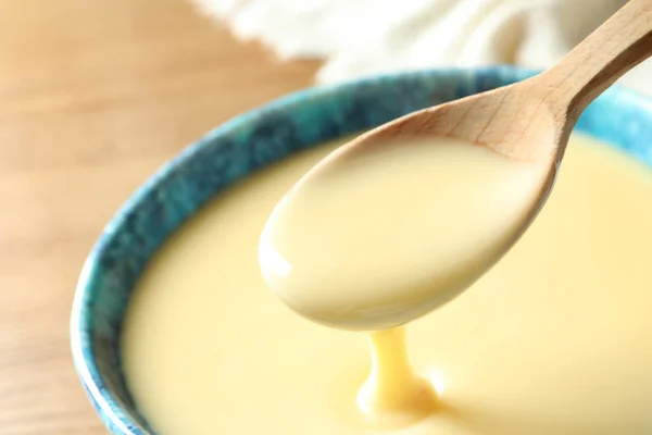Spoon of pouring condensed milk over bowl on table, closeup with space for text. Dairy products — Stock Photo, Image