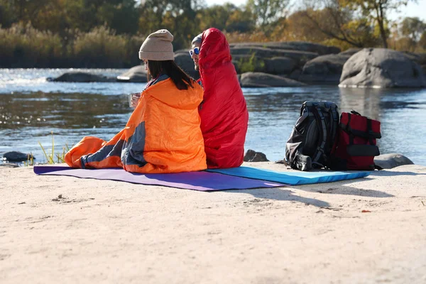 Campers sitting in sleeping bags on wild beach