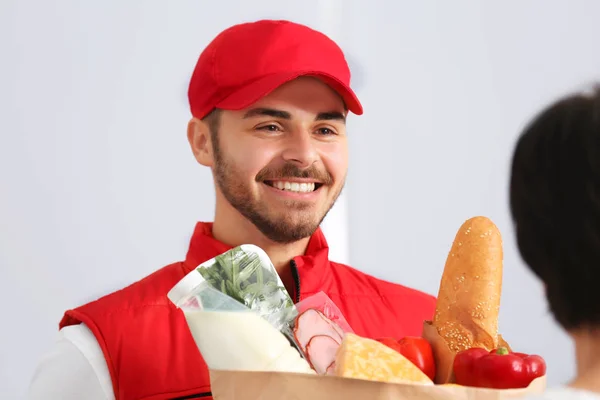 Male courier delivering food to client on light background — Stock Photo, Image