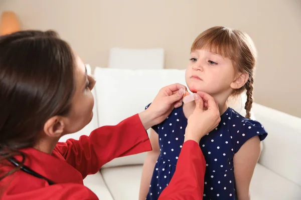 Nurse applying medical patch to little girl's injured face indoors. First aid — Stock Photo, Image