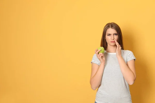 Emotionele jonge vrouw met gevoelige tanden en apple op kleur achtergrond. Ruimte voor tekst — Stockfoto