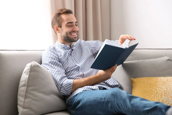 Przystojny, młody człowiek, czytając książkę na kanapie w domu — Zdjęcie stockowe