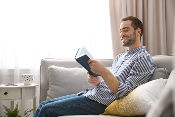 Przystojny, młody człowiek, czytając książkę na kanapie w domu — Zdjęcie stockowe