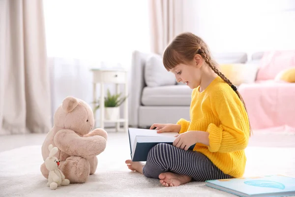 Aranyos kis lány mackó könyvével emeleten otthon — Stock Fotó